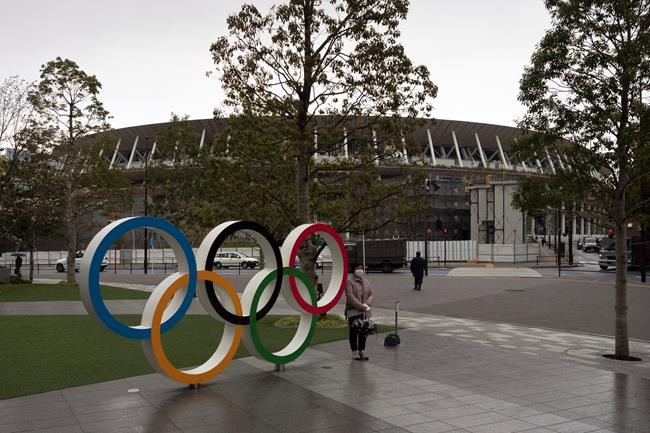A woman pauses for photos next to the Olympic rings near the New National Stadium in Tokyo, Monday, March 23, 2020. The IOC will take up to four weeks to consider postponing the Tokyo Olympics amid mounting criticism of its handling of the coronavirus crisis that now includes a call for delay from the leader of track and field, the biggest sport at the games. (AP Photo/Jae C. Hong)