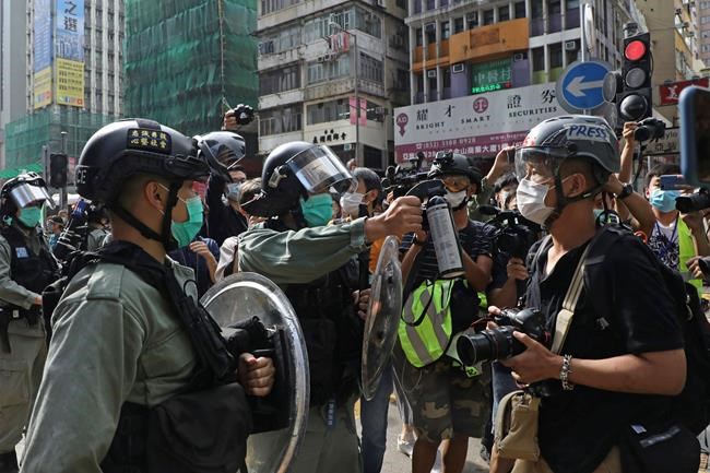 A riot police points the pepper spray to journalists as pro-democracy activists gather outside a shopping mall during the Labor Day in Hong Kong, Friday, May 1, 2020 amid an outbreak of the new coronavirus. May Day usually brings rallies and celebrations rallies marking international Labor Day. This year it's a bitter reminder of how much has been lost for the millions left idle or thrown out of work thanks to the coronavirus pandemic. (AP Photo/Kin Cheung)
