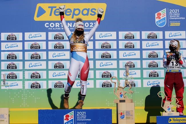 Switzerland's Corinne Suter celebrates on the podium after she won the gold medal in the women's downhill, at the alpine ski World Championships in Cortina d'Ampezzo, Italy, Saturday, Feb. 13, 2021. At right is bronze medal Switzerland's Lara Gut-Behrami. (AP Photo/Giovanni Auletta)