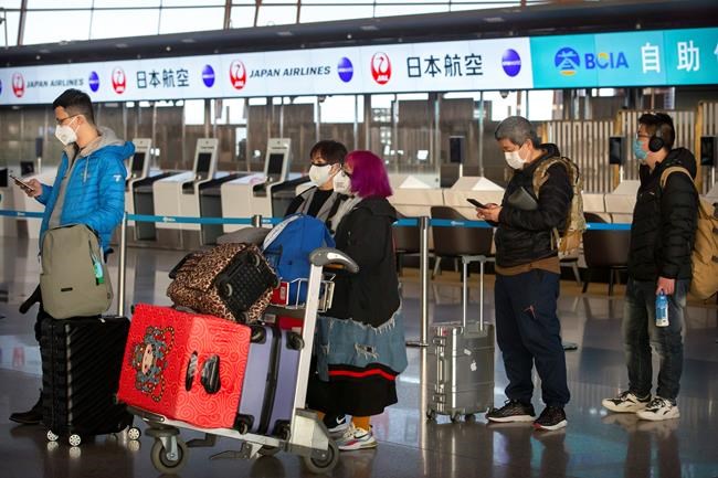 Travelers wearing face masks line up near the Japan Airlines check-in counters at Beijing Capital International Airport in Beijing, Thursday, Jan. 30, 2020. China counted 170 deaths from a new virus Thursday and more countries reported infections, including some spread locally, as foreign evacuees from China's worst-hit region returned home to medical observation and even isolation. (AP Photo/Mark Schiefelbein)