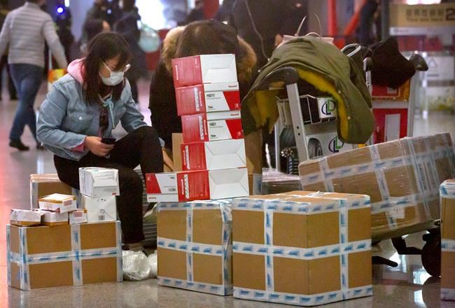 A traveler sits near boxes of face masks and respirators at the Beijing Capital International Airport in Beijing, Thursday, Jan. 30, 2020. China counted 170 deaths from a new virus Thursday and more countries reported infections, including some spread locally, as foreign evacuees from China's worst-hit region returned home to medical observation and even isolation. (AP Photo/Mark Schiefelbein)