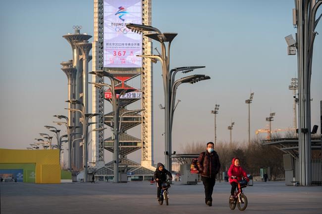 People walk on the Olympic Green near a countdown clock showing slightly more than 1 year to go for the 2022 Beijing Olympics in Beijing, Tuesday, Feb. 2, 2021. A coalition of 180 rights group on Wednesday called for a boycott of next year's Beijing Winter Olympics tied to reported human rights abuses against ethnic minorities in China. (AP Photo/Mark Schiefelbein)