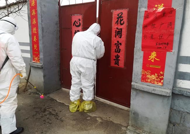 In this Saturday, Feb. 1, 2020, photo, government workers in protective suits visit a family under home quarantine in Zouping in eastern China's Shandong Province. The sing on the right reads:
