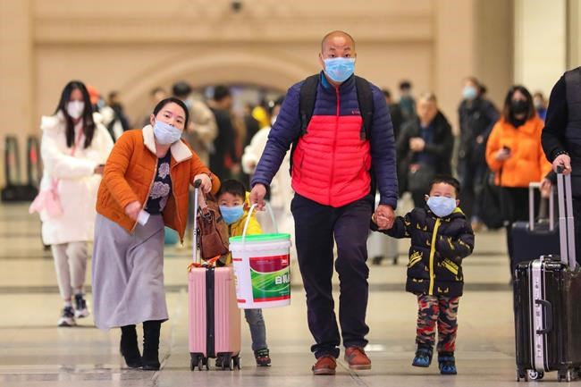 In this Tuesday, Jan. 21, 2020, photo, travelers wearing face masks walk with their luggage at Hankou Railway Station in Wuhan in southern China's Hubei province. The U.S. on Tuesday reported its first case of a new and potentially deadly virus circulating in China, saying a Washington state resident who returned last week from the outbreak's epicenter was hospitalized near Seattle. (Chinatopix via AP)