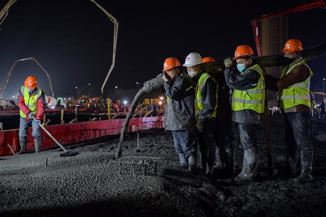 In this Tuesday, Jan. 28, 2020, photo, construction workers labor at the site of the Huoshenshan temporary field hospital being built in Wuhan in central China's Hubei Province. China as of Wednesday has more infections of a new virus than it did in with SARS, though the death toll is still lower. (Chinatopix via AP)