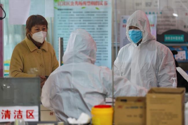 Medical workers in protective gear talk with a woman suspected of being ill with a coronavirus at a community health station in Wuhan in central China's Hubei Province, Monday, Jan. 27, 2020. China on Monday expanded sweeping efforts to contain a viral disease by extending the Lunar New Year holiday to keep the public at home and avoid spreading infection. (Chinatopix via AP)