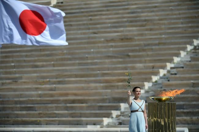 Choreographer Artemis Ignatiou stands next to the Olympic flame during the Olympic flame handover ceremony for the 2020 Tokyo Summer Olympics, in Athens, Thursday March 19, 2020. (Aris Messinis/Pool via AP)