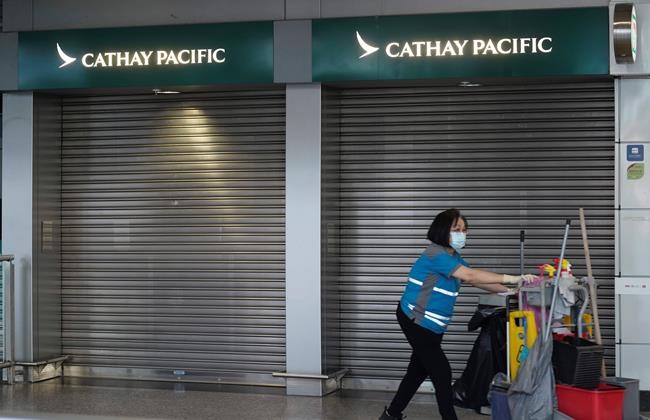 A cleaner walks past a Cathay Pacific booth at the airport train station in Hong Kong Wednesday, Oct. 21, 2020. Hong Kong airline Cathay Pacific Airways on Wednesday said it would cut 8,500 jobs and shut down its regional airline unit in a corporate restructuring, as it grapples with the plunge in air travel due to the pandemic. (AP Photo/Vincent Yu)