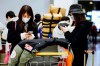Travelers from Beijing, wearing masks, use their cellphone as they arrive at Charles de Gaulle airport, north of Paris, early Monday, Jan. 27, 2020. France's government announced Sunday it will repatriate up to hundreds of French citizens from the Chinese city of Wuhan, the epicenter of a deadly new virus. (AP Photo/Kamil Zihnioglu)