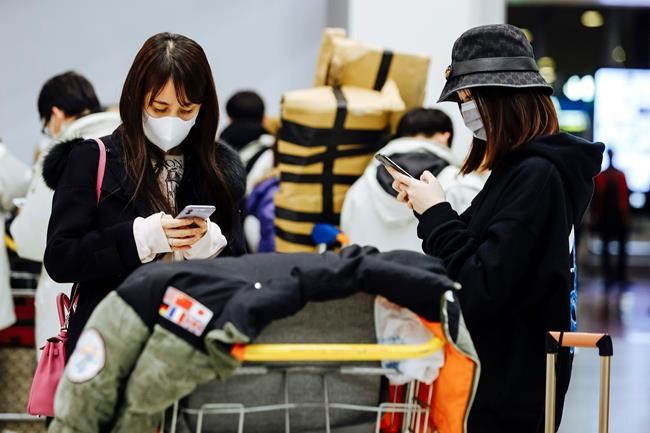 Travelers from Beijing, wearing masks, use their cellphone as they arrive at Charles de Gaulle airport, north of Paris, early Monday, Jan. 27, 2020. France's government announced Sunday it will repatriate up to hundreds of French citizens from the Chinese city of Wuhan, the epicenter of a deadly new virus. (AP Photo/Kamil Zihnioglu)