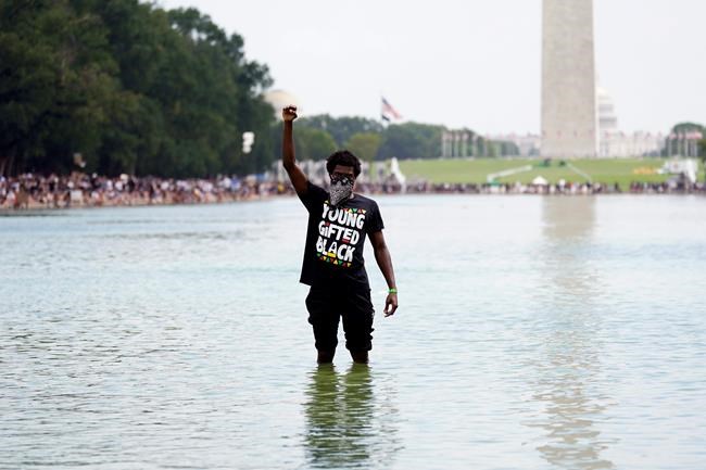 A man stands in the Reflecting Pool as people attend the March on Washington, Friday Aug. 28, 2020, in Washington, on the 57th anniversary of the Rev. Martin Luther King Jr.'s