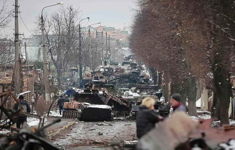 People look at the gutted remains of Russian military vehicles on a road in the town of Bucha, close to the capital Kyiv, Ukraine, Tuesday, March 1, 2022. Russia on Tuesday stepped up shelling of Kharkiv, Ukraine's second-largest city, pounding civilian targets there. Casualties mounted and reports emerged that more than 70 Ukrainian soldiers were killed after Russian artillery recently hit a military base in Okhtyrka, a city between Kharkiv and Kyiv, the capital. (AP Photo/Serhii Nuzhnenko)