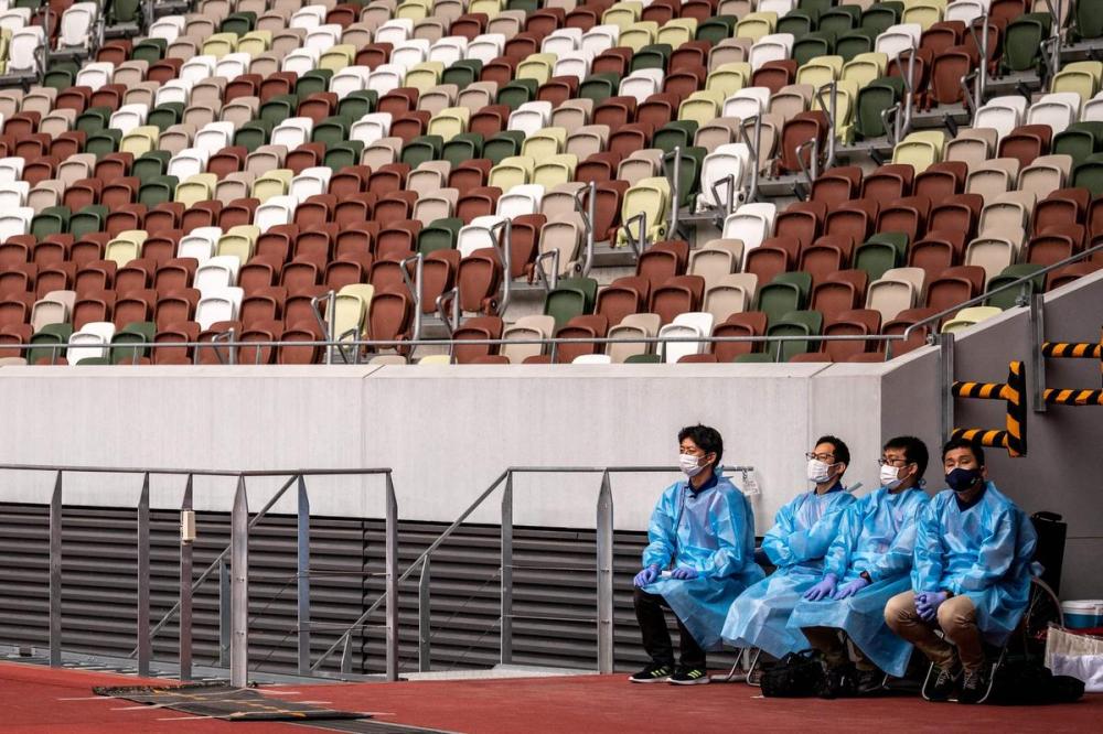 PHILIP FONG - AFP via GETTY IMAGES
This file photo taken on May 11, 2021 shows staff members in protective clothing and masks standing by next to empty seats during a para-athletics test event for the 2020 Tokyo Olympics at the National Stadium in Tokyo. - Tokyo's Olympics will be like no other Games, with the spectre of coronavirus hanging over every part of the event, and organisers determined to prevent an outbreak.