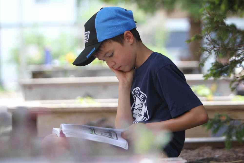Leif in grade 2 enjoys reading his comic book in the shade during lunch break.