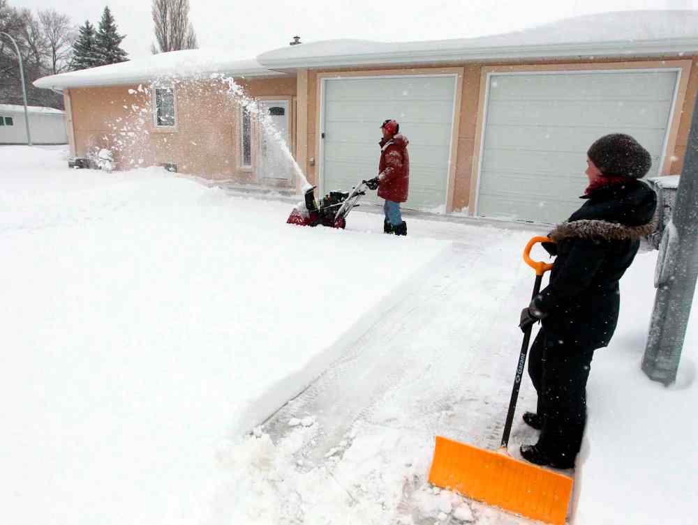 Kim Barrow, with yellow push shovel, is happy that her neighbour on Cormorant Bay, Bob Yamashita, has a gas powered snowblower. (Boris Minkevich / Winnipeg Free Press)