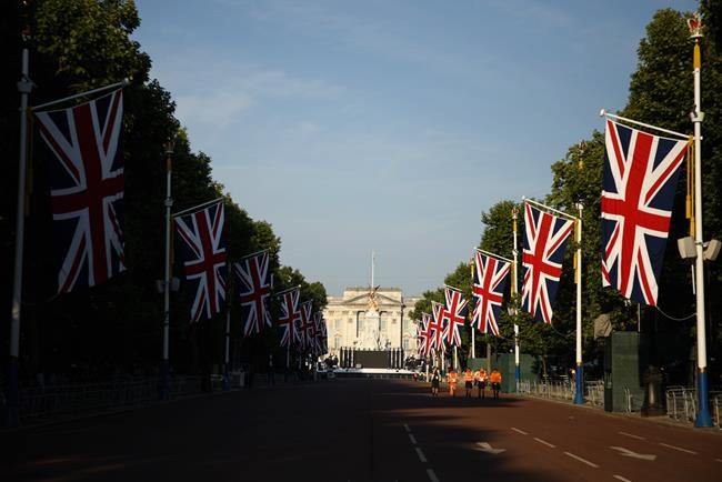 A handful of workers walk down the Mall leading to Buckingham Palace in London, Thursday June 2, 2022, on the first of four days of celebrations to mark the Platinum Jubilee. The events over a long holiday weekend in the U.K. are meant to celebrate the monarch's 70 years of service. (AP Photo/David Cliff)
