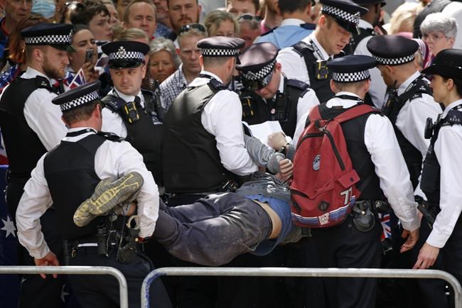 Police officers remove a man who ran into the path of the royal procession on The Mall, London, ahead of the Trooping the Color ceremony in London, Thursday June 2, 2022, on the first of four days of celebrations to mark the Platinum Jubilee. The events over a long holiday weekend in the U.K. are meant to celebrate the monarch's 70 years of service. (AP Photo/David Cliff)