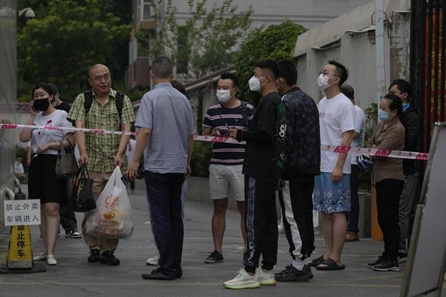Residents wearing face masks stand watch behind a barricaded tape set up in their locked down apartment buildings for health monitoring following a COVID-19 case detected in the area in Beijing, Thursday, June 9, 2022. (AP Photo/Andy Wong)