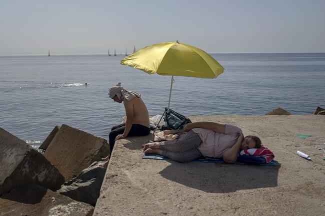 A woman sleeps under an umbrella on a breakwater in front of the Mediterranean Sea in Barcelona, Spain, Thursday, June 16, 2022. Spain's weather service says a mass of hot air from north Africa is triggering the country's first major heat wave of the year with temperatures expected to rise to 43 degrees Celsius (109.4 degrees Fahrenheit) in certain areas. (AP Photo/Emilio Morenatti)
