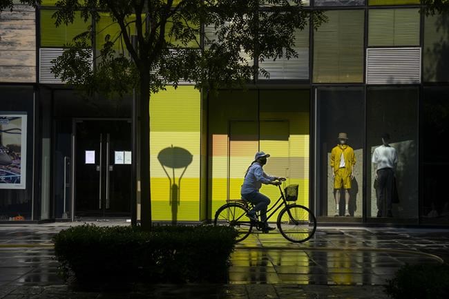 FILE - A woman wearing a face mask rides a bicycle past stores closed for COVID-19 control at a shopping mall in Beijing, Tuesday, May 17, 2022. Neither inflation nor the war in Ukraine are threatening to take a bite out of the luxury fashion market, according to a study published Tuesday, June 21, 2022. (AP Photo/Mark Schiefelbein, File)