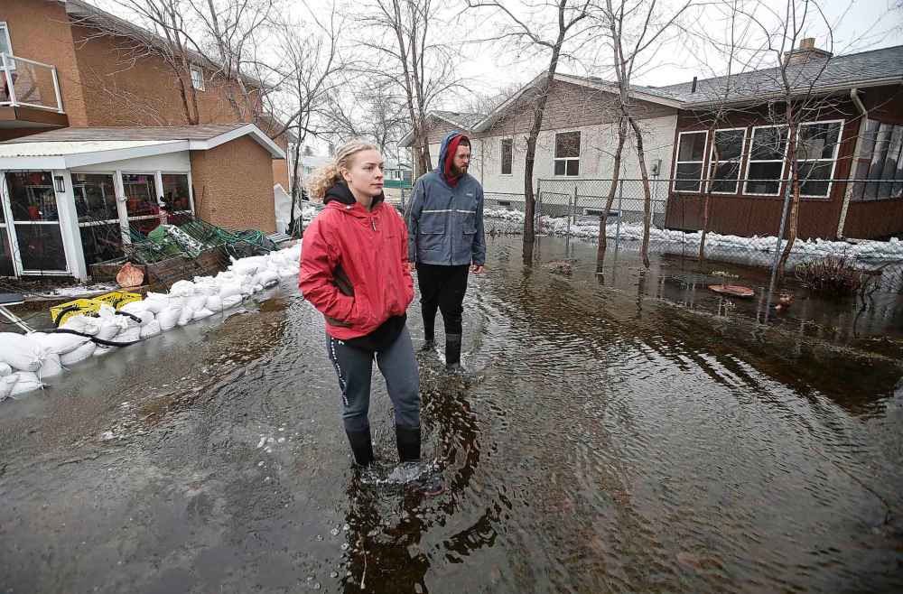 Cameryn Johnson and Brett Hanslit survey the water surrounding their home after a railway ditch overflowed its banks and flooded their property on Rizzuto Bay Sunday. (John Woods / Winnipeg Free Press)