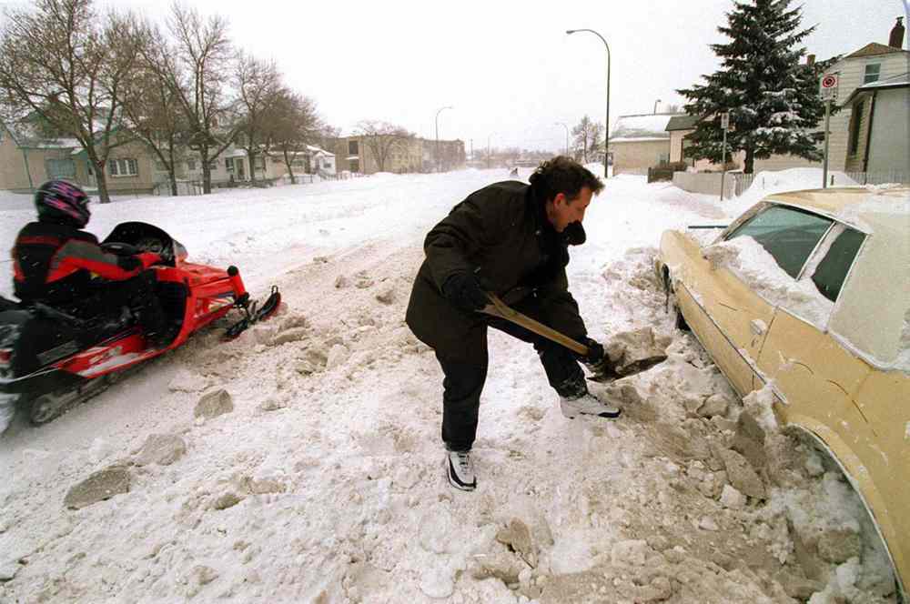 As a snowmobile passes, Winnipegger Rick Tanchuk digs out his car that was buried by a passing snowplow on McPhillips Street near Burrows Avenue. (Jeff DeBooy / Winnipeg Free Press files)