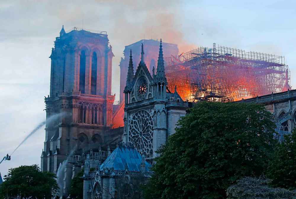 A firefighter tackles the blaze as flames and smoke rise from Notre Dame cathedral as it burns. (Michel Euler / The Associated Press)