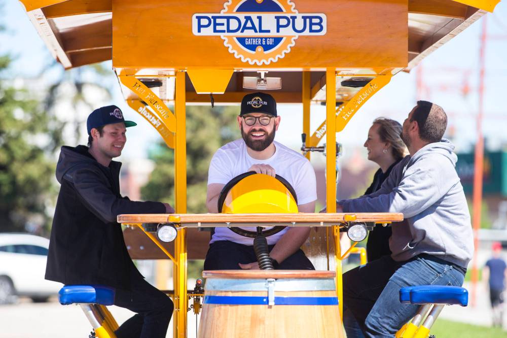 Pedal Pub co-owner Miguel Gauthier (driver, centre) demonstrates the rig, along with co-owner Brandon Guenther (left), general manager Randi Davreux, and co-owner Rylan Adam. The party bike has a sober guide to control the direction and speed of the vehicle. (Mikaela MacKenzie / Winnipeg Free Press)