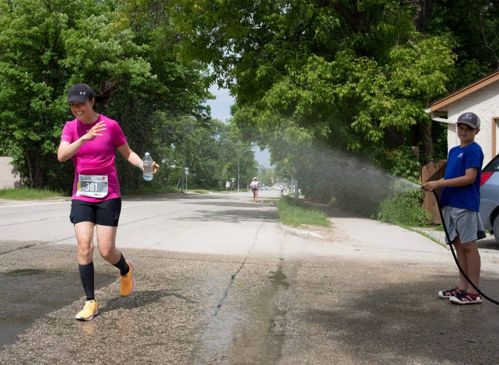 At right, 10-year-old Erik Dear offers a helpful spraying of water to passing Manitoba Marathon runners. (Jessica Lee / Winnipeg Free Press)