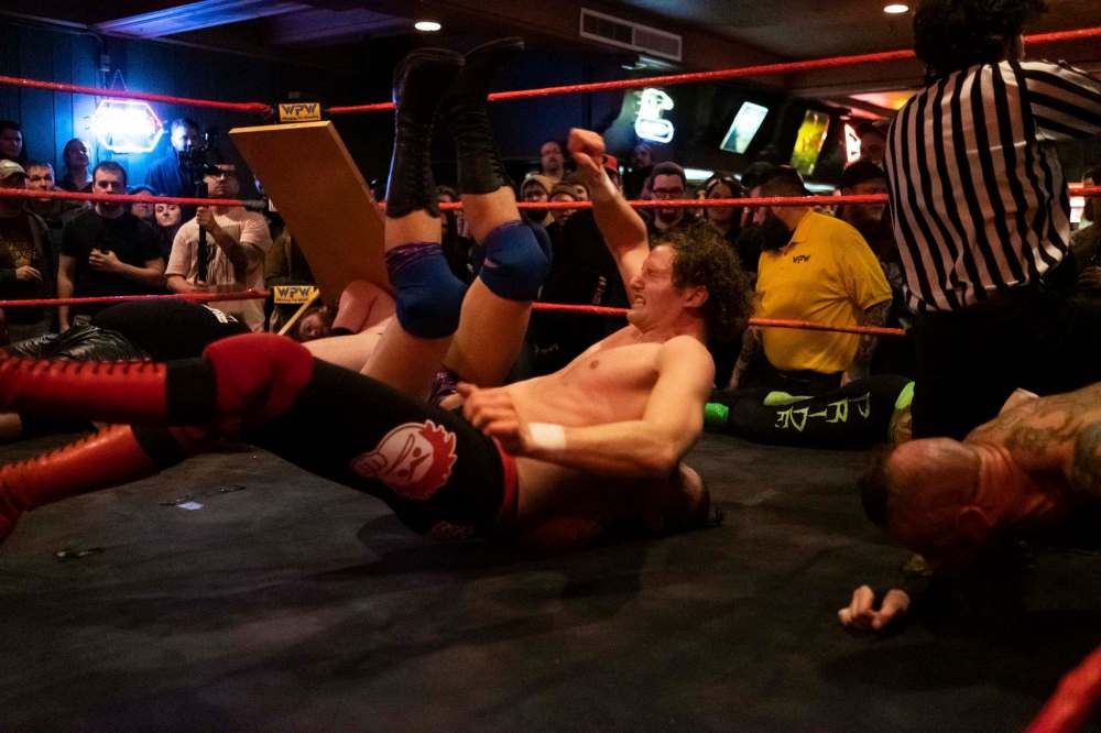 Bobby Shink slams his opponent onto the ring during a six-man match -.