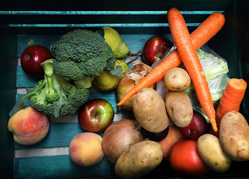 A crate half loaded with fresh fruits and veggies. More items will still go into the crate.