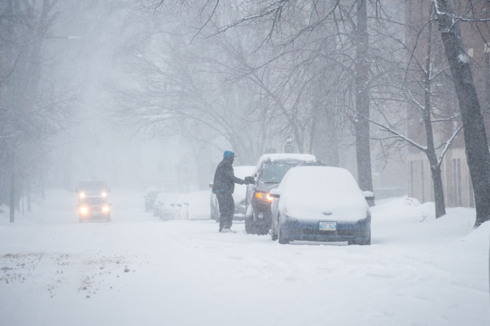 A man sweeps snow off of his car parked on Edmonton Street in Winnipeg during a spring snowstorm. (Mike Sudoma / The Canadian Press)