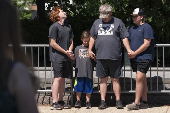 Wearing an anti-abortion T-shirt, a father and his sons from Central Florida pray, as abortion-rights supporters protest outside of the Supreme Court, Wednesday, June 29, 2022, in Washington. (AP Photo/Jacquelyn Martin)