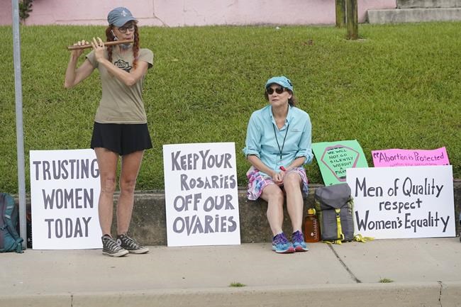 Abortion rights supporter Elli Morris, left, played her bamboo flute outside the Jackson Women's Health Organization clinic in Jackson, Miss., as she and others carried signs expressing their opinions, Saturday, July 2, 2022. The clinic is the only facility that performs abortions in the state. On June 24, the U.S. Supreme Court overturned Roe v. Wade, ending constitutional protections for abortion. However, a Mississippi judge has set a hearing for Tuesday, in a lawsuit by the state's only abortion clinic that seeks to block a law that would ban most abortions. (AP Photo/Rogelio V. Solis)