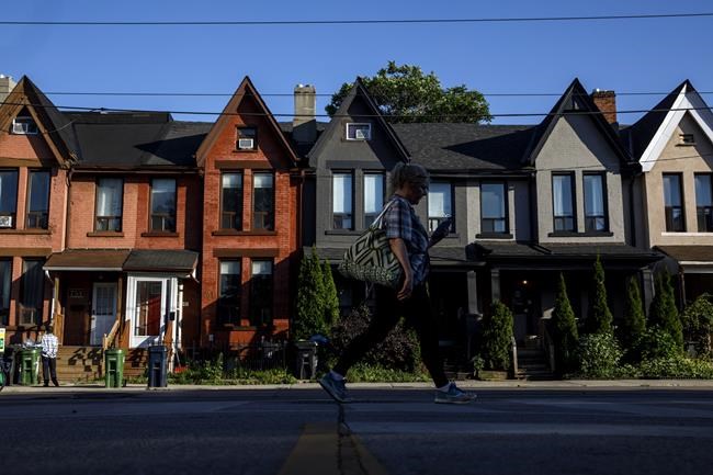 A person walks by a row of houses in Toronto on Tuesday July 12, 2022. The Bank of Canada increased its key interest rate by one percentage point Wednesday in the largest hike the country has seen in 24 years.THE CANADIAN PRESS/Cole Burston
