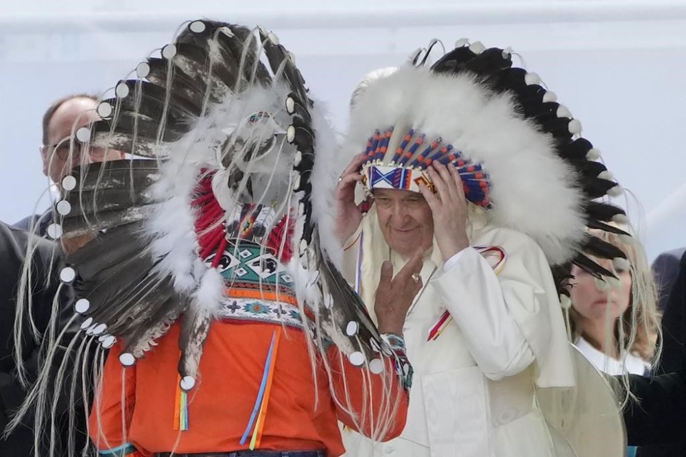 Pope Francis puts on an indigenous headdress during a meeting with indigenous communities, including First Nations, Metis and Inuit, at Our Lady of Seven Sorrows Catholic Church in Maskwacis, near Edmonton, Canada, Monday, July 25, 2022. Pope Francis begins a