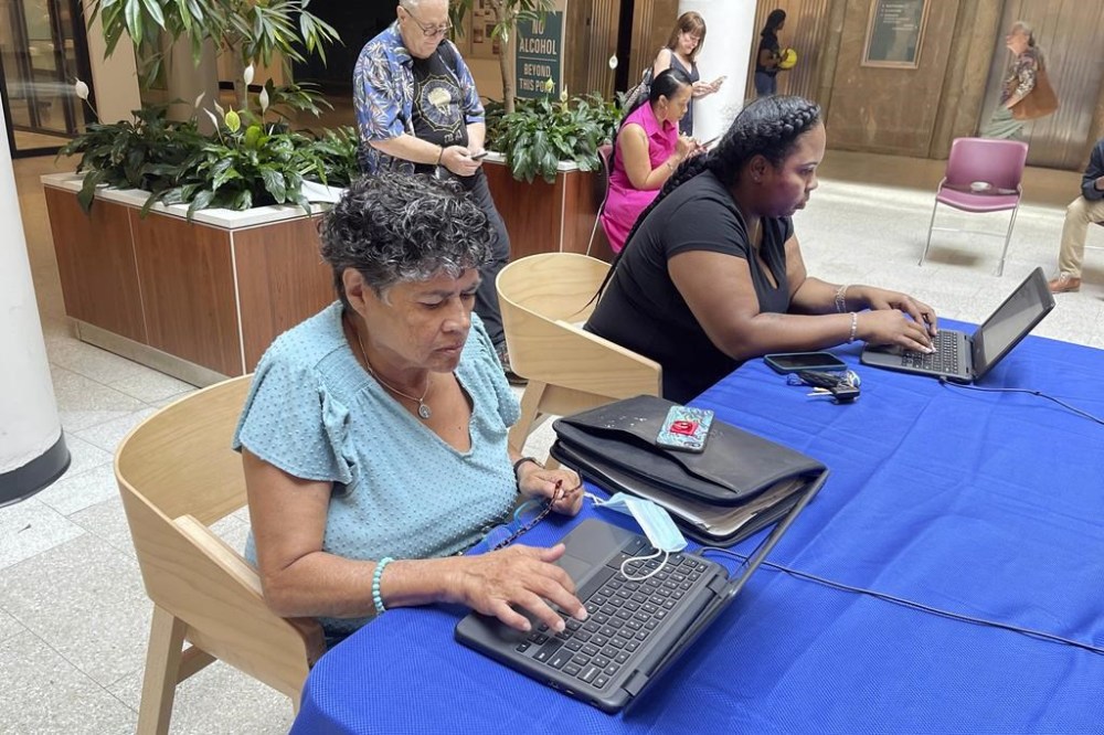 Carmen Cruz, of Greece, N.Y., foreground, a Rochester City School District teacher applicant, applies with others during a recruitment event at the Mercantile On Main, in Rochester, NY, Wednesday, Aug. 17, 2022. She's been a substitute teacher and was hoping her bilingual background would help her get a permanent teaching position. (AP Photo/Carolyn Thompson)