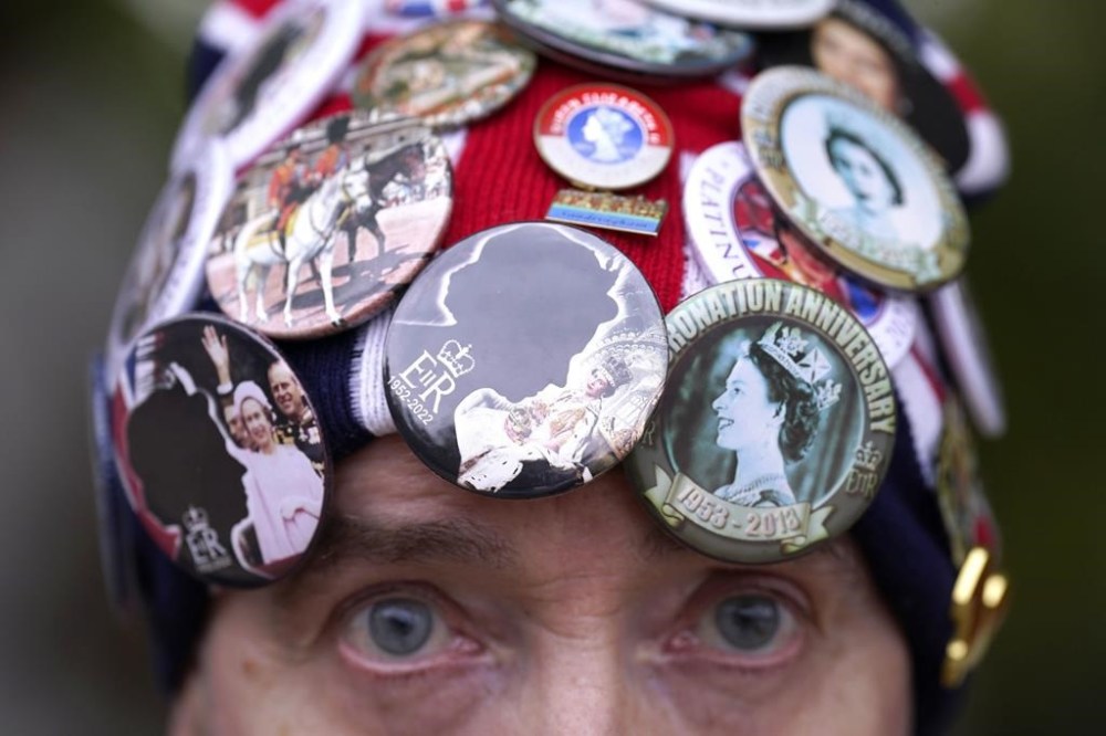 John Loughrey, wearing a hat with various badges of Queen Elizabeth II, is seen outside Buckingham Palace in London, Tuesday, Sept. 13, 2022. After lying in St. Giles' Cathedral in the historic heart of Edinburgh Monday night and through most of Tuesday, Queen Elizabeth II's coffin will be flown back to London and driven to her official London home, Buckingham Palace. (Danny Lawson/PA via AP)