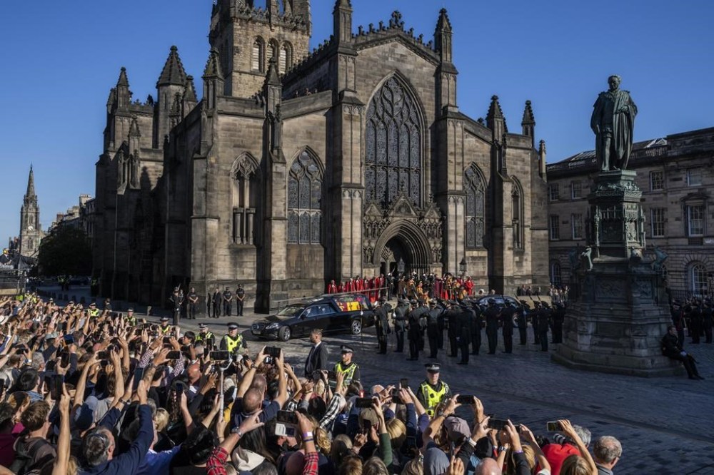 People take photos with their mobile phones as the Queens cortege with the hearse carrying Queen Elizabeth's coffin departs from St Giles Cathedral en route to Edinburgh Airport in Edinburgh, Scotland, Tuesday, Sept. 13, 2022. After lying in the cathedral most of Tuesday, the queen's coffin will be flown back to London and driven to her official London home, Buckingham Palace. (AP Photo/Bernat Armangue)
