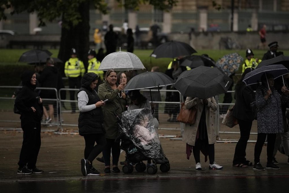 People line the road waiting for a convoy carrying the coffin of late Queen Elizabeth II, heading towards Buckingham Palace in London, Tuesday, Sept. 13, 2022. Britain's longest-reigning monarch who was a rock of stability across much of a turbulent century, died Thursday Sept. 8, 2022, after 70 years on the throne. She was 96. (AP Photo/Andreea Alexandru)