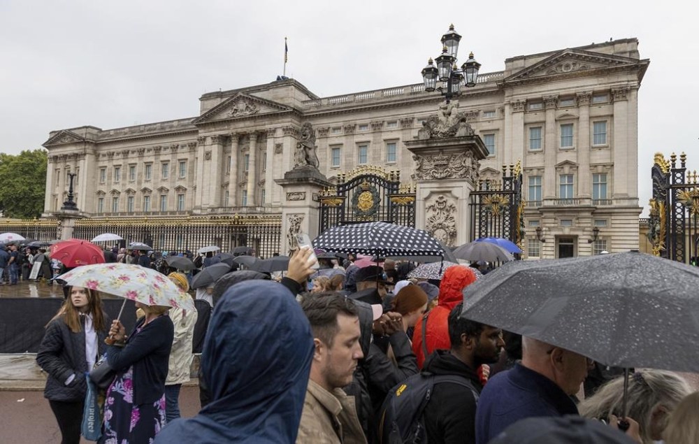 Members of the public gather in the rain outside Buckingham Palace, in London, ahead of the arrival of the hearse carrying the coffin of Queen Elizabeth II, Tuesday, Sept. 13, 2022. (Suzan Moore/Pool Photo via AP)