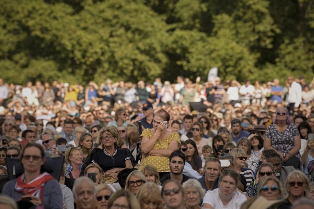A woman wipes away tears as she joins people sitting in Hyde Park, London, Wednesday, Sept. 14, 2022 watching screens broadcasting the procession of the coffin of Queen Elizabeth II from Buckingham Palace to Westminster Hall. The Queen will lie in state in Westminster Hall for four full days before her funeral on Monday Sept. 19. (AP Photo/Andreea Alexandru)