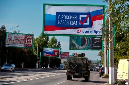 FILE - A military vehicle drives along a street with a billboard that reads: 