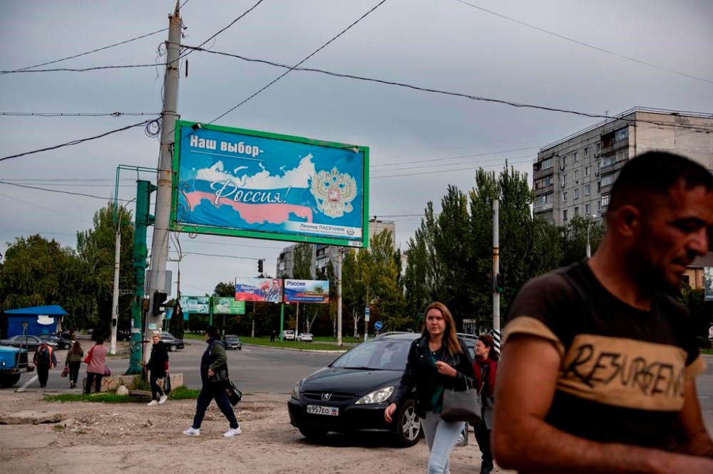 FILE - People walk in a street with a billboard that reads: