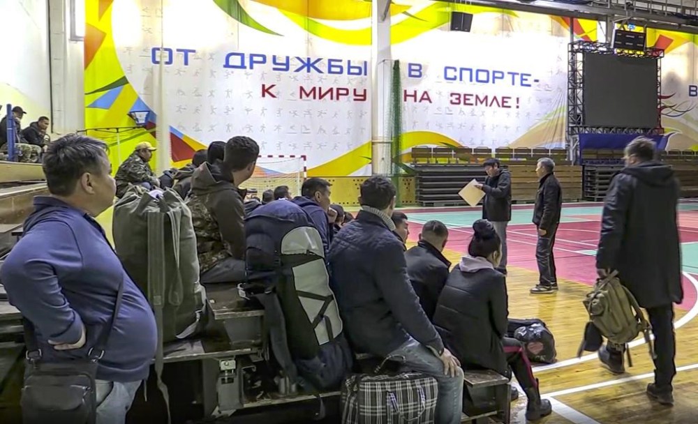 In this image taken from video, Russian draftees gather inside an indoor stadium turned into collection center for the draftees, who will be sent to the military units of the Eastern Military District, in Yakutsk, Russia, Friday, Sept. 23, 2022. Mobilization is underway in Russia's Far Eastern region of Yakutia after President Vladimir Putin ordered a partial mobilization of reservists Wednesday to bolster his forces in Ukraine. The words in the background read