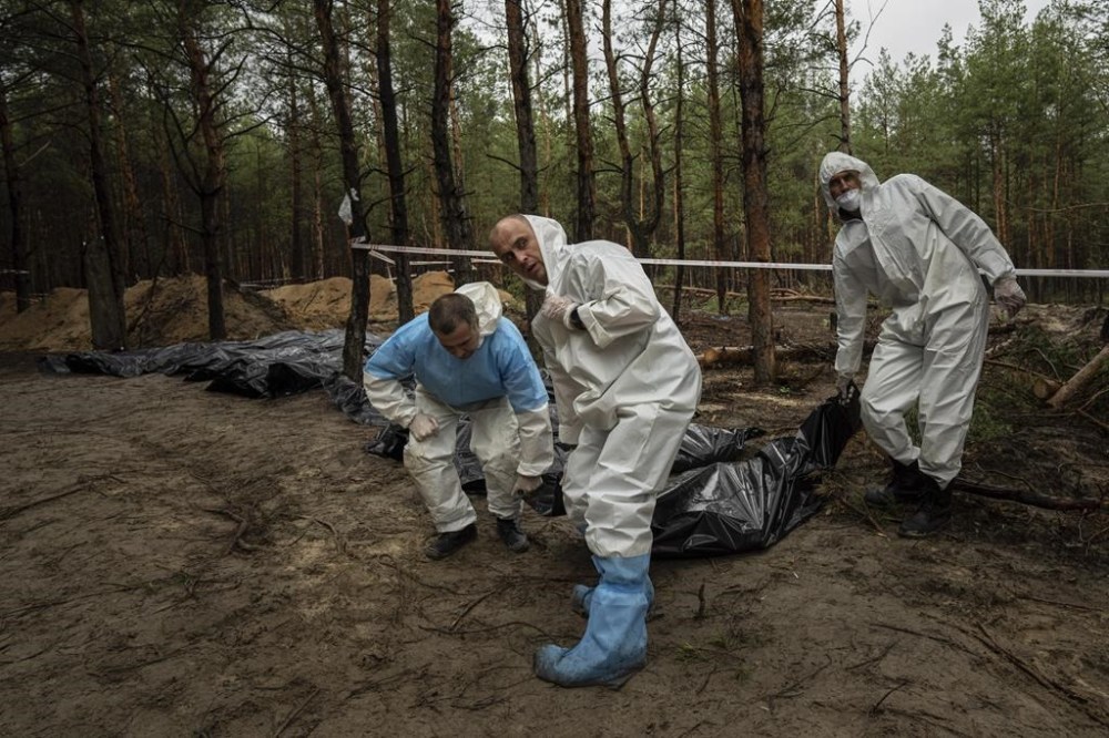 Emergency workers carry bodies to a refrigerator truck in a cemetery after exhumation in the recently retaken area of Izium, Ukraine, Friday, Sept. 23, 2022. (AP Photo/Evgeniy Maloletka)