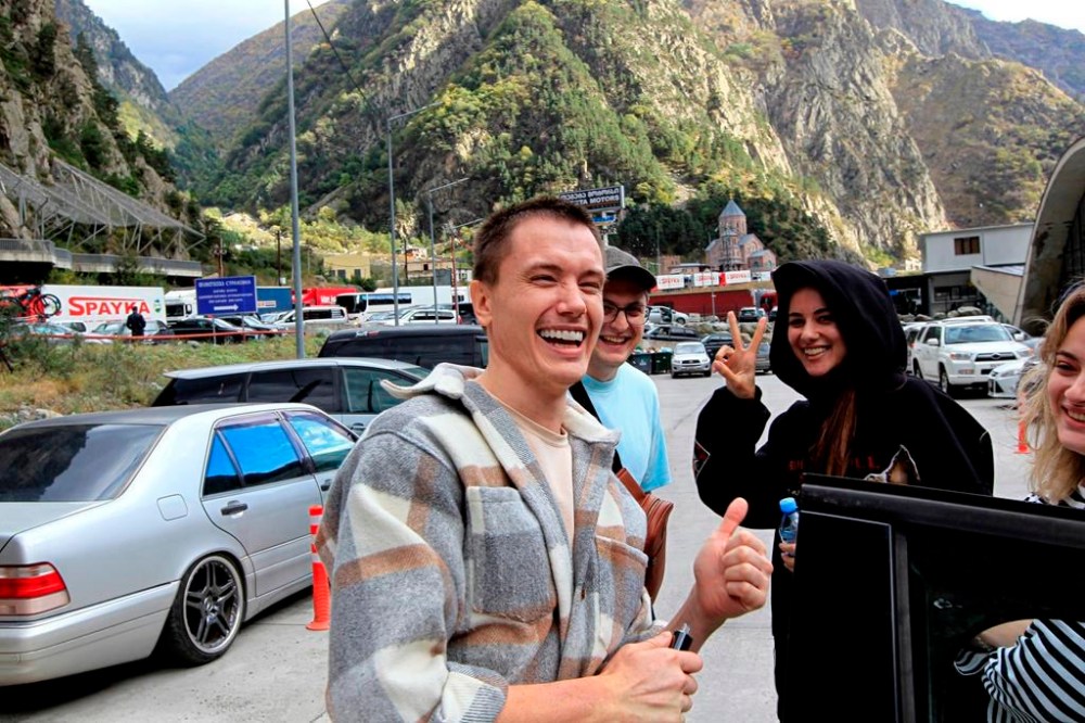 FILE A group of Russians smile at the border crossing Verkhny Lars between Georgia and Russia on Friday, Sept. 23, 2022. Long lines of vehicles have formed at a border crossing between Russia's North Ossetia region and Georgia after Moscow announced a partial military mobilization. A day after President Vladimir Putin ordered a partial mobilization to bolster his troops in Ukraine, many Russians are leaving their homes. (AP Photo/Shakh Aivazov, File)