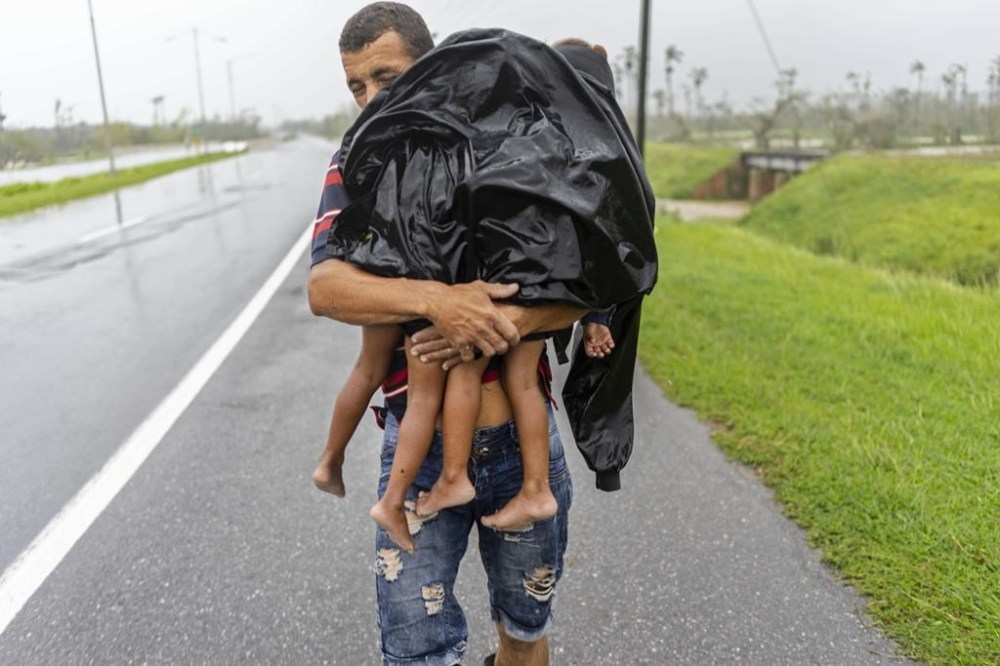A man carries two children in the rain in search of shelter after Hurricane Ian flooded their home in Pinar del Rio, Cuba, Tuesday, Sept. 27, 2022. Ian made landfall at 4:30 a.m. EDT Tuesday in Cuba’s Pinar del Rio province, where officials set up shelters, evacuated people, rushed in emergency personnel and took steps to protect crops in the nation’s main tobacco-growing region. (AP Photo/Ramon Espinosa)