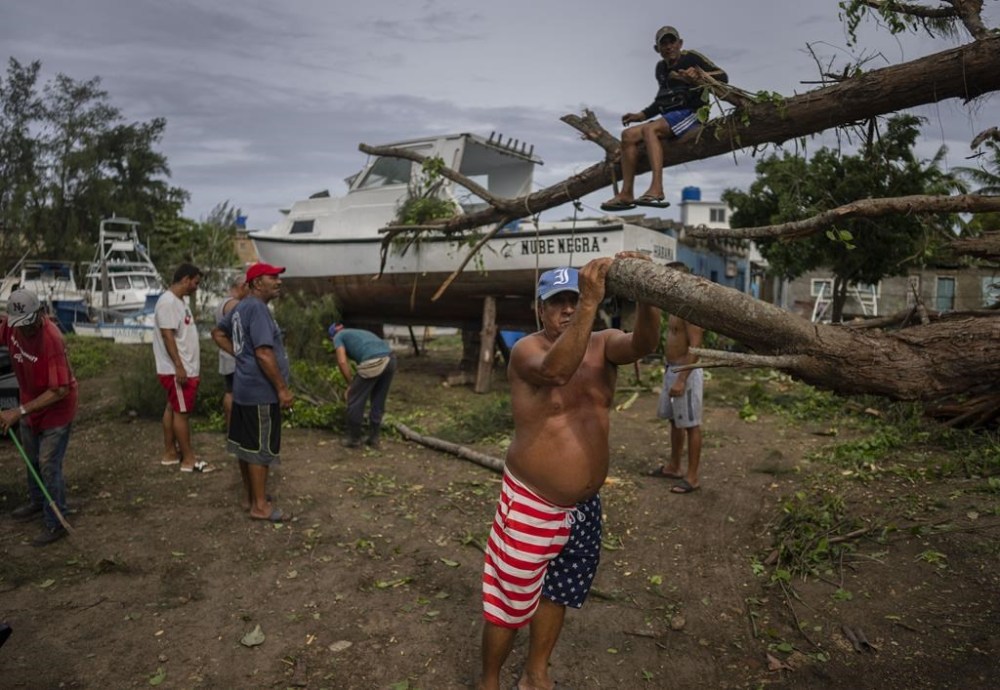 People rest as they cut down a tree that fell on top of a boat due to Hurricane Ian in Havana, Cuba, Wednesday, Sept. 28, 2022. Cuba remained in the dark early Wednesday after Ian knocked out its power grid and devastated some of the country's most important tobacco farms when it hit the island's western tip as a major storm. (AP Photo/Ramon Espinosa)