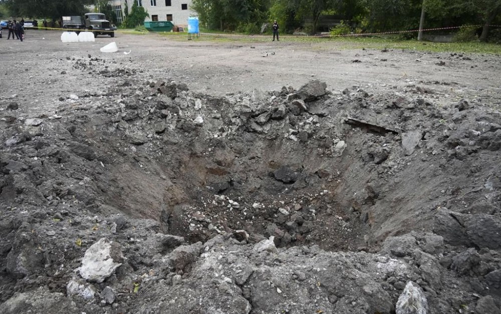 A police officer stands next to a crater created by an explosion after a Russian rocket attack in Zaporizhzhia, Ukraine, Friday, Sept. 30, 2022. A Russian strike on the Ukrainian city of Zaporizhzhia killed at least 23 people and wounded dozens, an official said Friday. Vladimir Putin's claim to parts of Ukraine is little more than